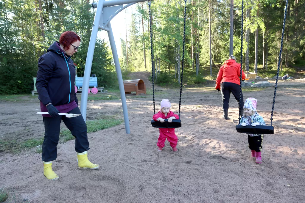 Frida Santala ja Eveliina Lahti odottavat keinujen luona, kun perhepäivähoitajat Tanja Kuuhimo ja Elina Kierikka puhdistavat hiekan kissojen jätöksistä.